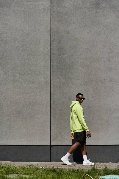 Stylish African American man in yellow hoodie walking by gray wall. — Stock Photo