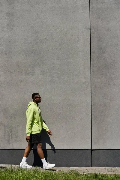 A fashionable young African American man walking in front of a gray wall. — Stock Photo