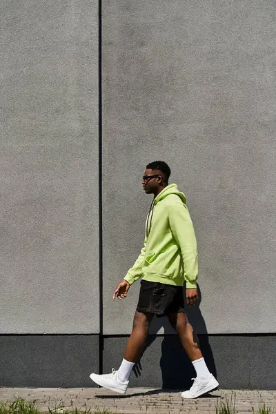 Modischer afroamerikanischer Mann in grünem Kapuzenpulli läuft die Straße entlang. — Stockfoto