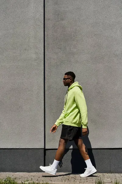 Fashionable African American male in green hoodie walking down street. — Stock Photo