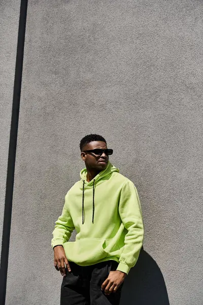Stylish African American man in lime green hoodie leaning against a wall. — Stock Photo