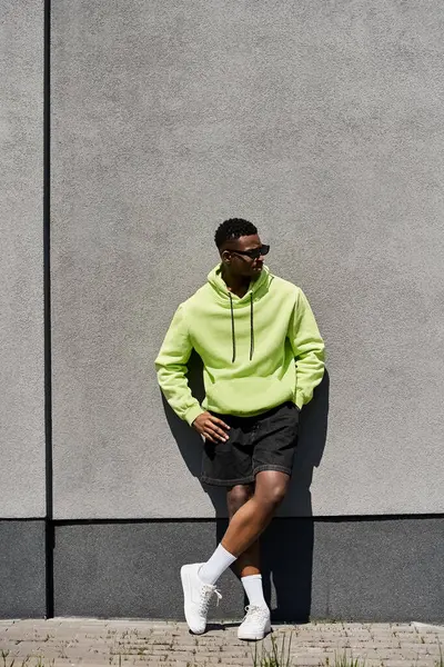 Handsome African American man in lime hoodie leaning against wall. — Stock Photo