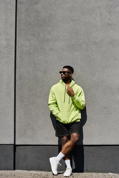 Homme afro-américain élégant en sweat à capuche vert appuyé contre un mur. — Photo de stock