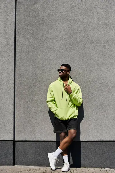 Elegante hombre afroamericano con capucha verde apoyado contra una pared. — Stock Photo