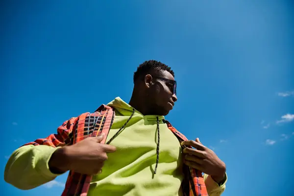 Un jeune homme afro-américain à la mode dans une veste jaune se tient devant un ciel bleu vibrant. — Photo de stock
