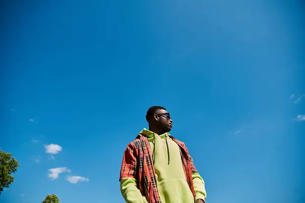 Ein modischer afroamerikanischer Mann steht auf einem Feld unter blauem Himmel. — Stockfoto