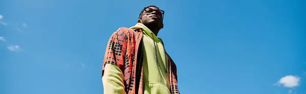 A stylish young African American man in a colorful jacket standing high in the sky. — Stock Photo
