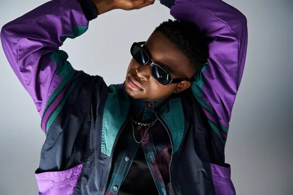Handsome African American male in fashionable purple jacket stands with hands on head. — Stock Photo