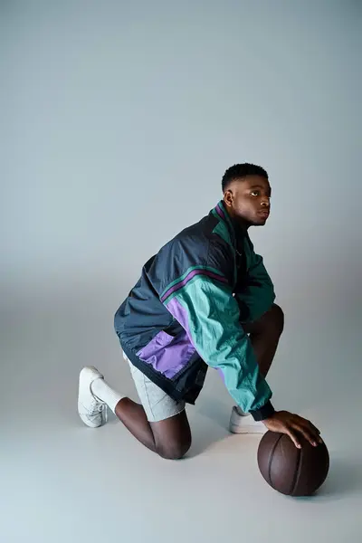 Афроамериканец в стильной одежде, приседающий с баскетболом. — стоковое фото