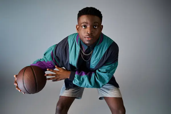 Stylish young African American man holding a basketball against a gray background. — Stock Photo