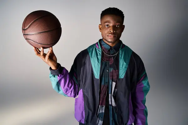 Fashionable African American man holding basketball against gray background. — Stock Photo