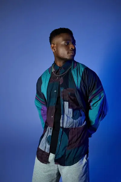 Стильный афроамериканец в красочной куртке, позирует на ярком синем фоне. — стоковое фото