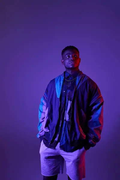 Handsome man in stylish jacket and shorts striking a pose in front of a vibrant purple background. — Stock Photo