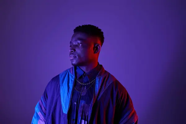 Handsome African American man poses in trendy blue jacket against vibrant purple backdrop. — Stock Photo