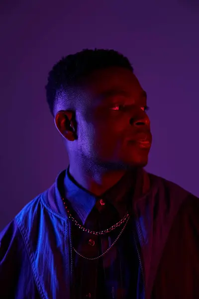 Handsome African American man in fashionable jacket and chain against vivid purple backdrop. — Stock Photo