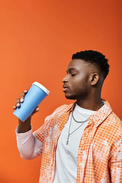 Handsome African American man sips from cup against vibrant orange backdrop. — Stock Photo
