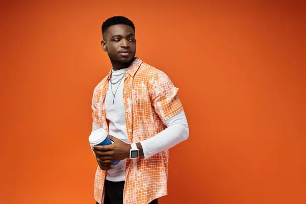 Ein modischer junger Afroamerikaner im orangefarbenen Hemd steht selbstbewusst vor einem dazu passenden orangefarbenen Hintergrund.. — Stockfoto