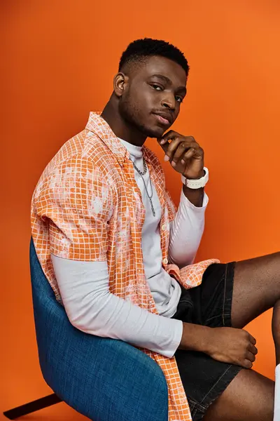 Handsome African American man in orange shirt sitting on chair. — Stock Photo