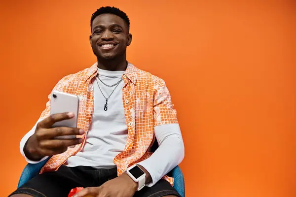 Handsome African American man in stylish attire sitting in a chair while using a cell phone. — Stock Photo