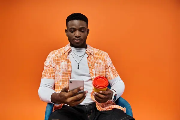 Young African American man sitting in chair, holding coffee cup. — Stock Photo
