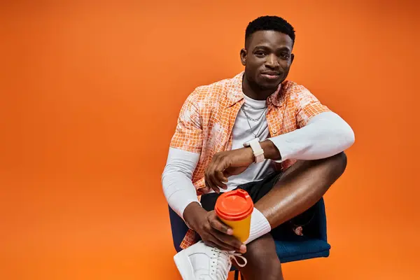 Young African American man in chic attire sits, holding coffee. — Stock Photo
