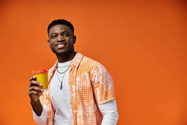 Bonito homem afro-americano desfrutando de uma xícara de café contra um cenário laranja brilhante. — Fotografia de Stock