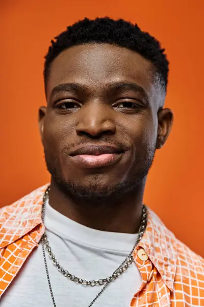 Handsome African American man looking fashionable in bright orange shirt and stylish chain accessory. — Stock Photo