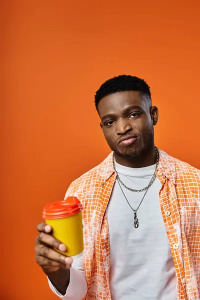 Young man holding coffee cup against vivid orange backdrop. — Stock Photo