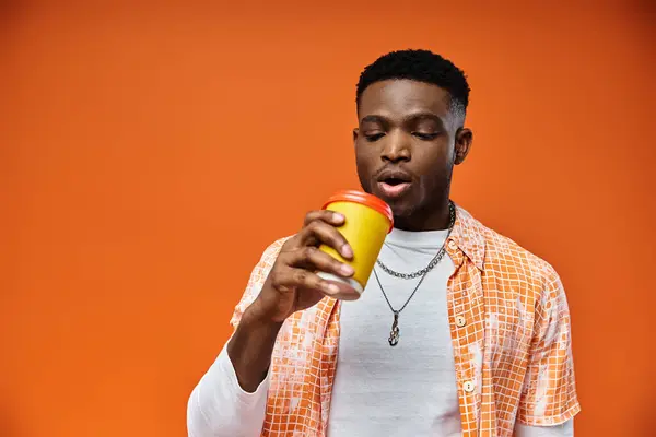 Young African American man drinking from a cup on orange background. — Stock Photo