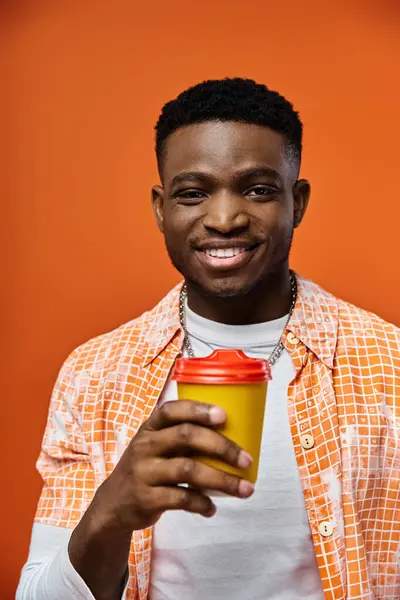 Handsome man enjoying coffee against vibrant orange backdrop. — Stock Photo