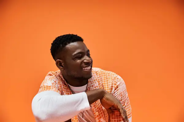 Handsome man in orange shirt striking a pose against orange backdrop. — Stock Photo