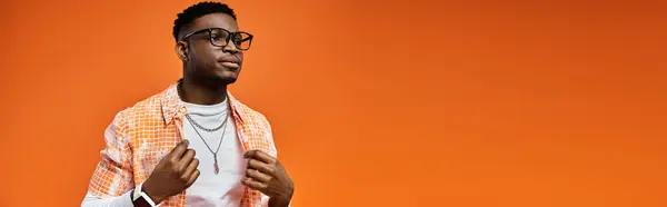 Handsome young African American man with glasses posing against bold orange backdrop. — Stock Photo
