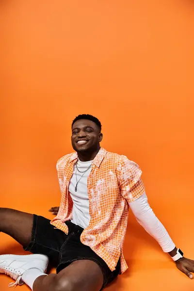 Fashionable African American man in orange shirt relaxing on bright orange background. — Stock Photo