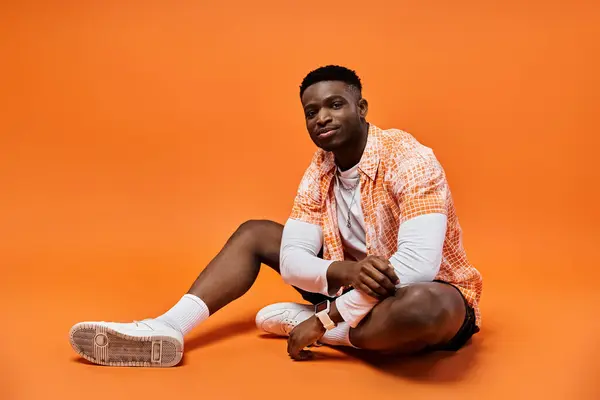 Bonito jovem afro-americano em elegante camisa laranja sentado graciosamente no chão. — Fotografia de Stock