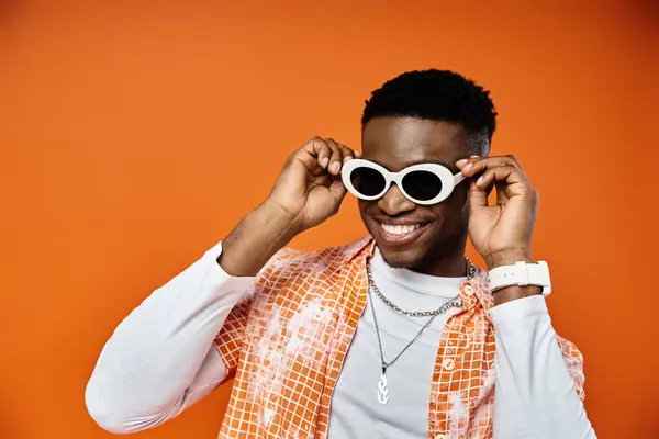 Young man in sunglasses on vibrant orange backdrop. — Stock Photo