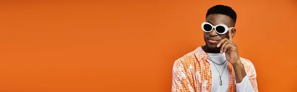 Schöner afroamerikanischer Mann mit trendiger Sonnenbrille auf leuchtend orangefarbenem Hintergrund. — Stockfoto