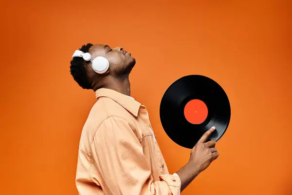 Schöner schwarzer Mann mit Kopfhörer hält Schallplatte vor leuchtend orangefarbenem Hintergrund. — Stockfoto