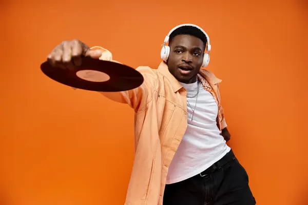 Elegante hombre negro con auriculares sosteniendo un registro sobre fondo naranja. - foto de stock