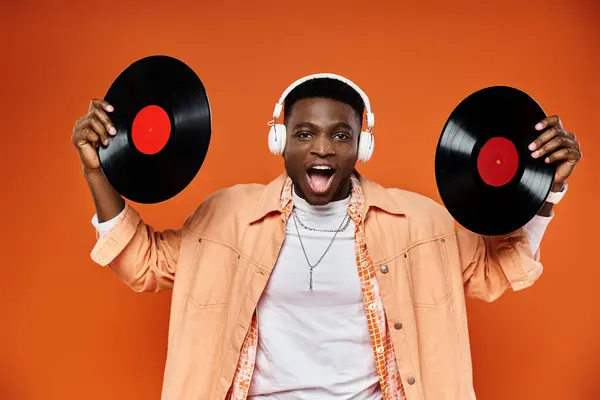 Stylish black man holding vinyl records against bright orange background. — Stock Photo