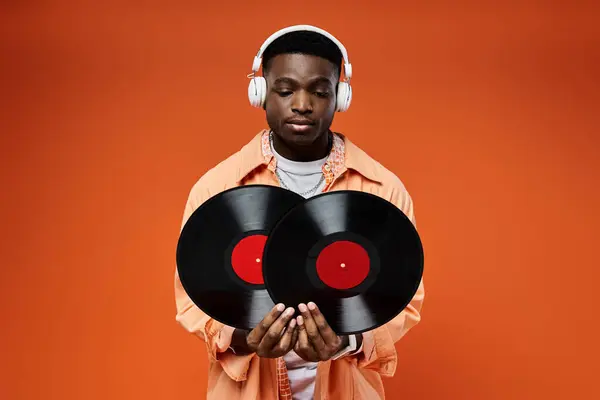 Handsome African American man in stylish attire holding a record and listening with headphones. — Stock Photo
