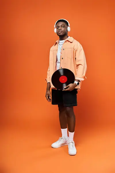 Fashionable African American man holds record on bright orange backdrop. — Stock Photo