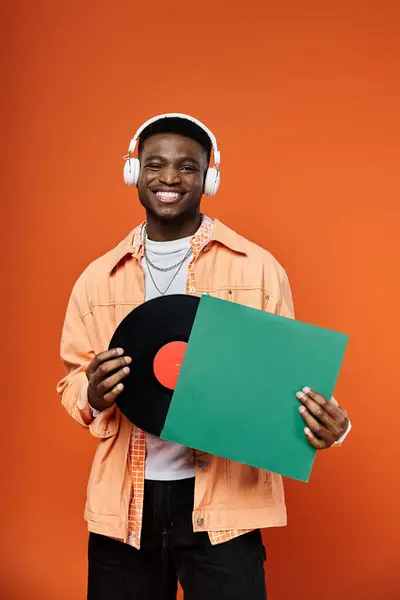 Schöner afroamerikanischer Mann in stylischer Kleidung, der eine Schallplatte mit Kopfhörern in der Hand hält. — Stockfoto