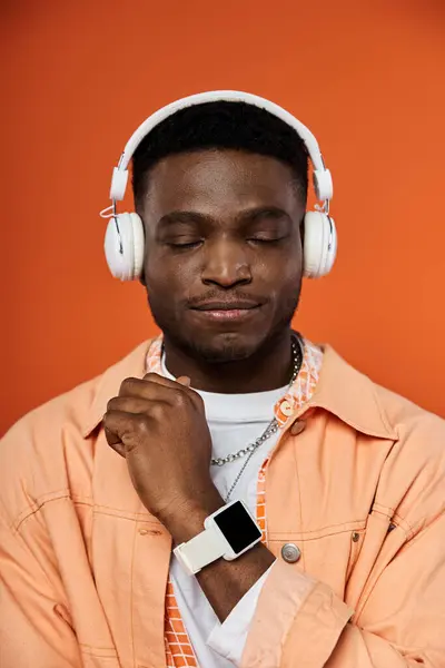 Stylish African American man in headphones against bright orange backdrop. — Stock Photo