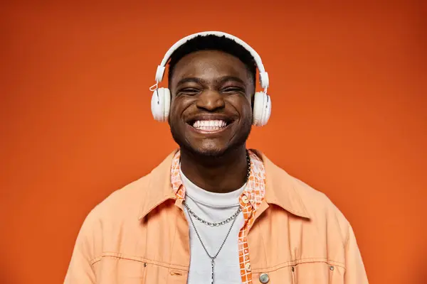 Handsome African American man with headphones beaming against orange backdrop. — Stock Photo