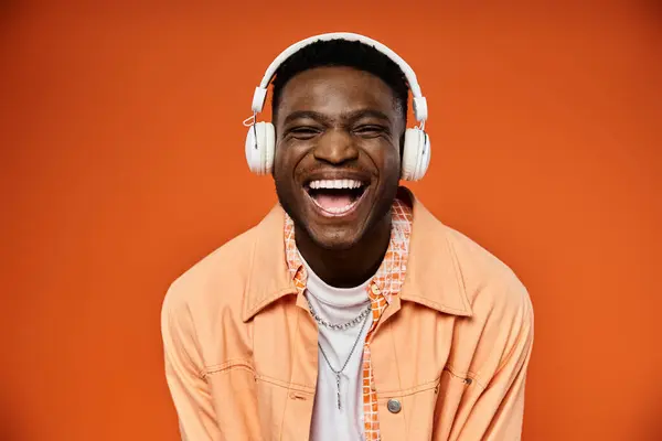 Stylish black man smiles wearing headphones on orange background. — Stock Photo