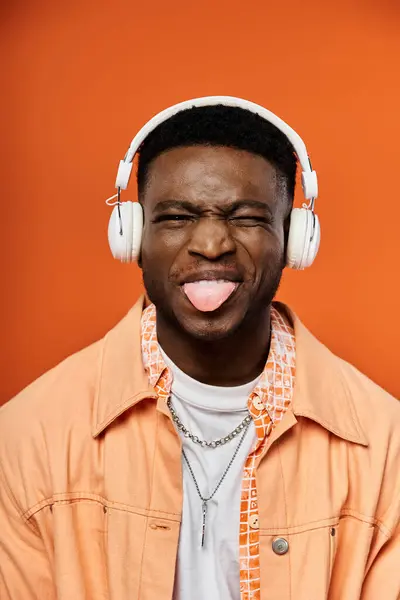 Стильний афроамериканський чоловік у навушниках з язиком, що стирчить у веселому та грайливому жесті. — стокове фото