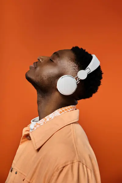 Stylish African American man in headphones on vibrant orange background. — Stock Photo