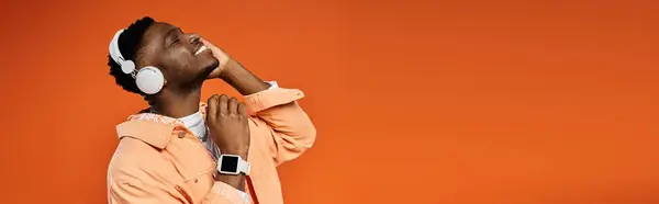 A fashionable young African American man in stylish attire holds his head up while listening to music. — Stock Photo