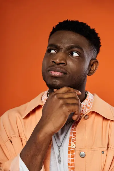 Handsome African American man in orange shirt, chin resting on hand. — Stock Photo