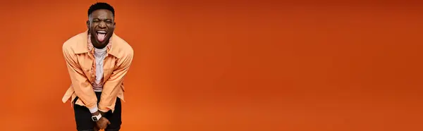 Fashionable African American man poses gracefully against bold orange background. — Stock Photo